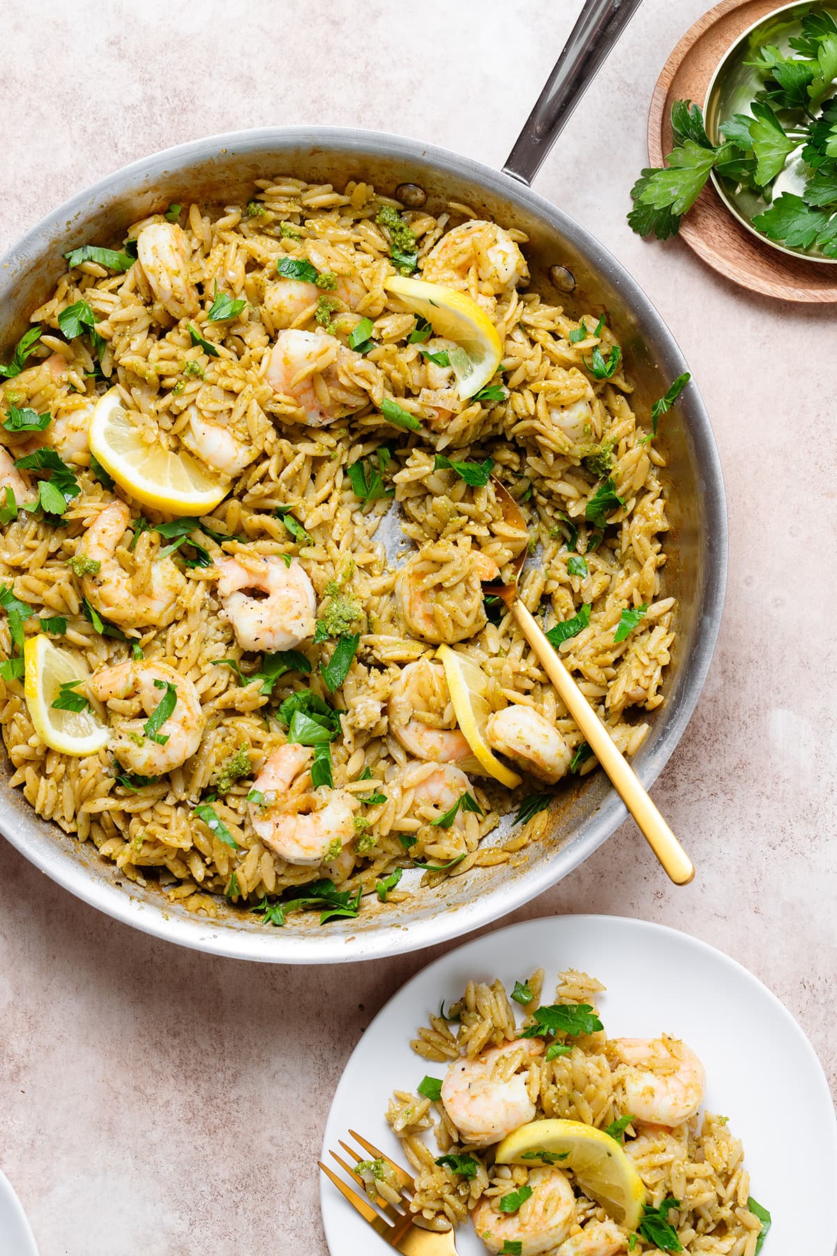 Pesto orzo with shrimp and slices of lemon in a large pan with a gold spoon resting on the right side of it.