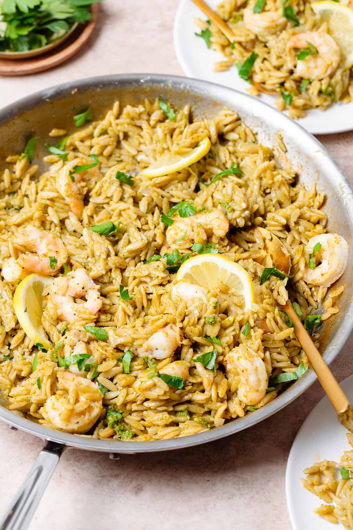 Pesto orzo with shrimp and slices of lemon in a large pan with a gold spoon resting on the right side of it.