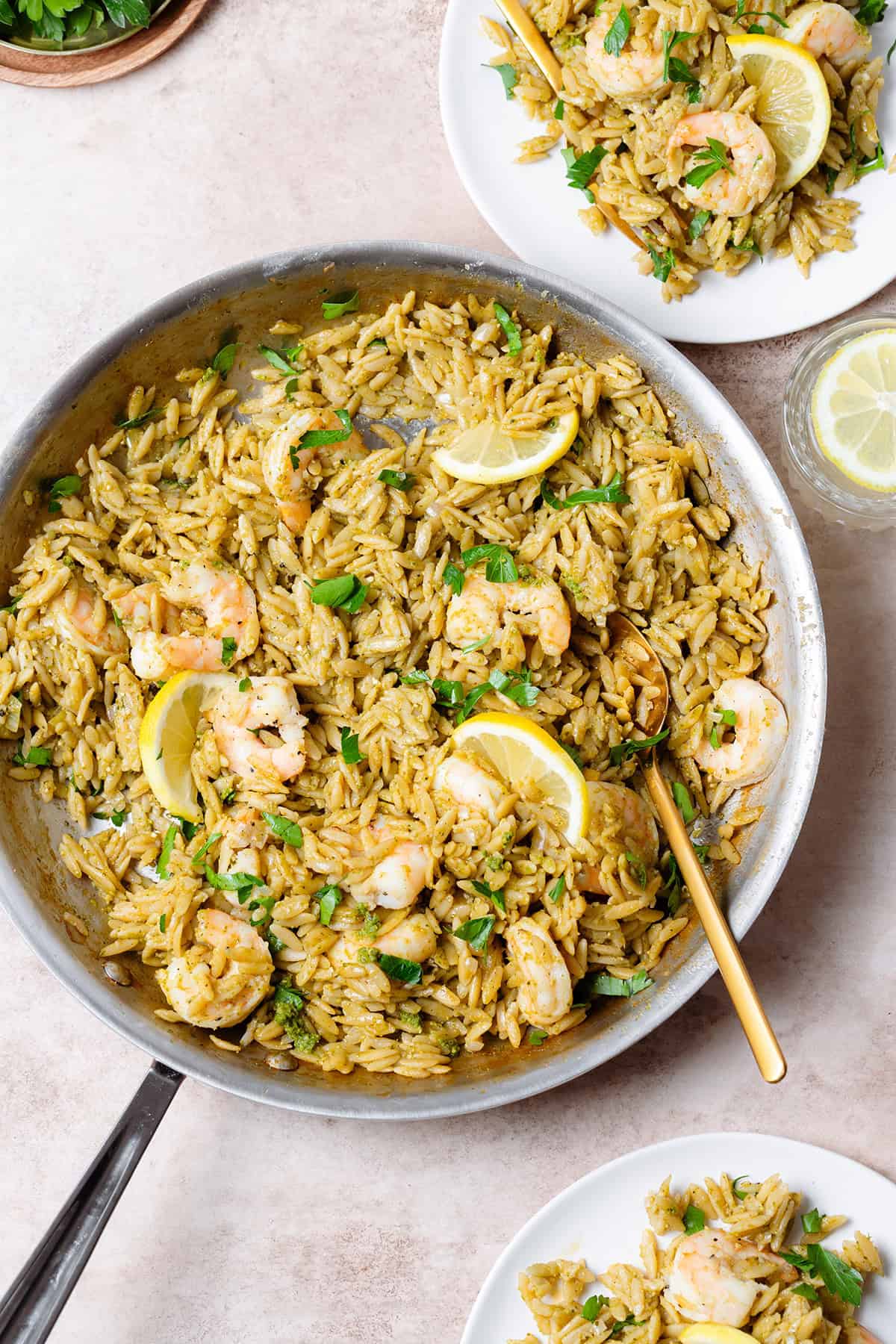 A large pan with cooked orzo with pesto, shrimp, and lemon slices.