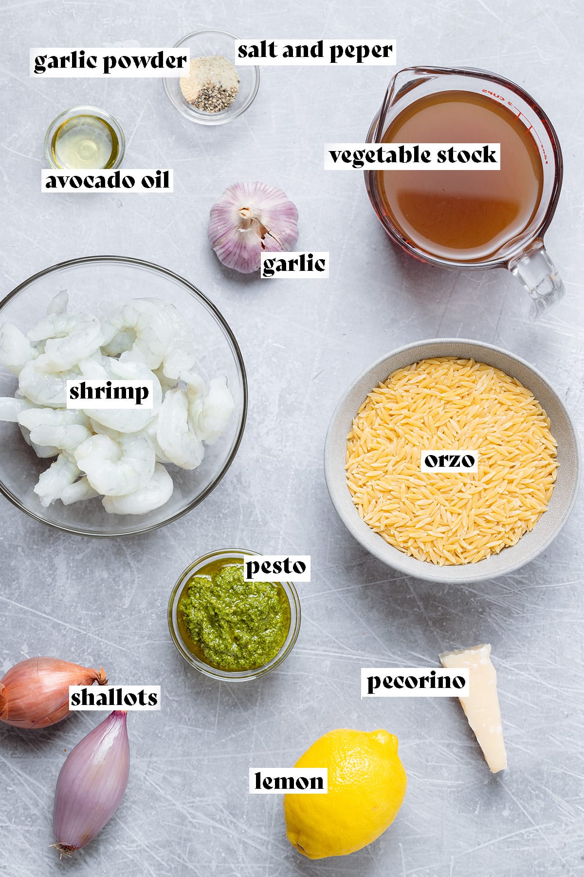 Ingredients for pesto orzo like raw shrimp, orzo, and vegetable stock all laid out on a metal background.
