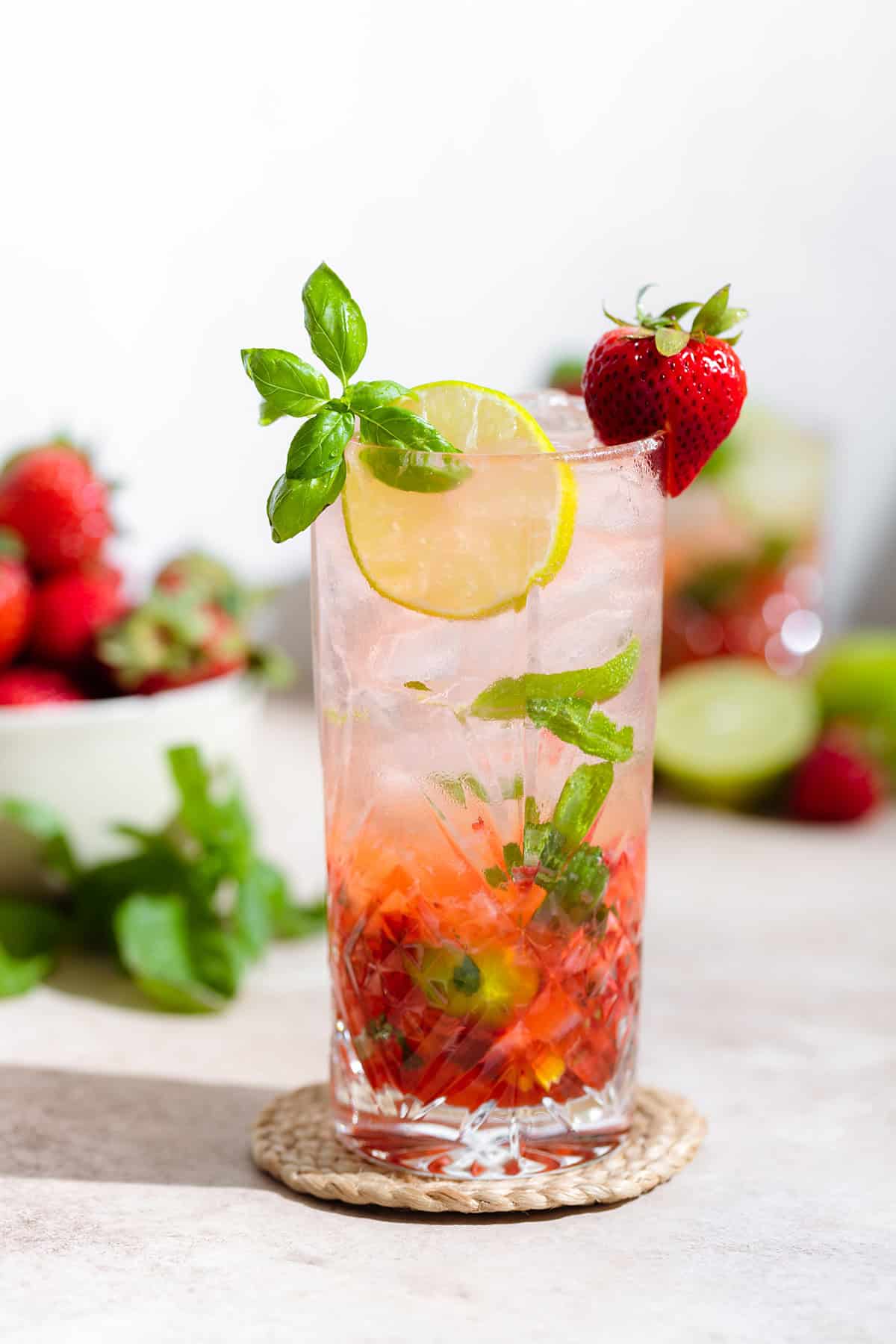 Strawberry basil mojito in a tall glass garnished with fresh basil, lime slice, and a strawberry.