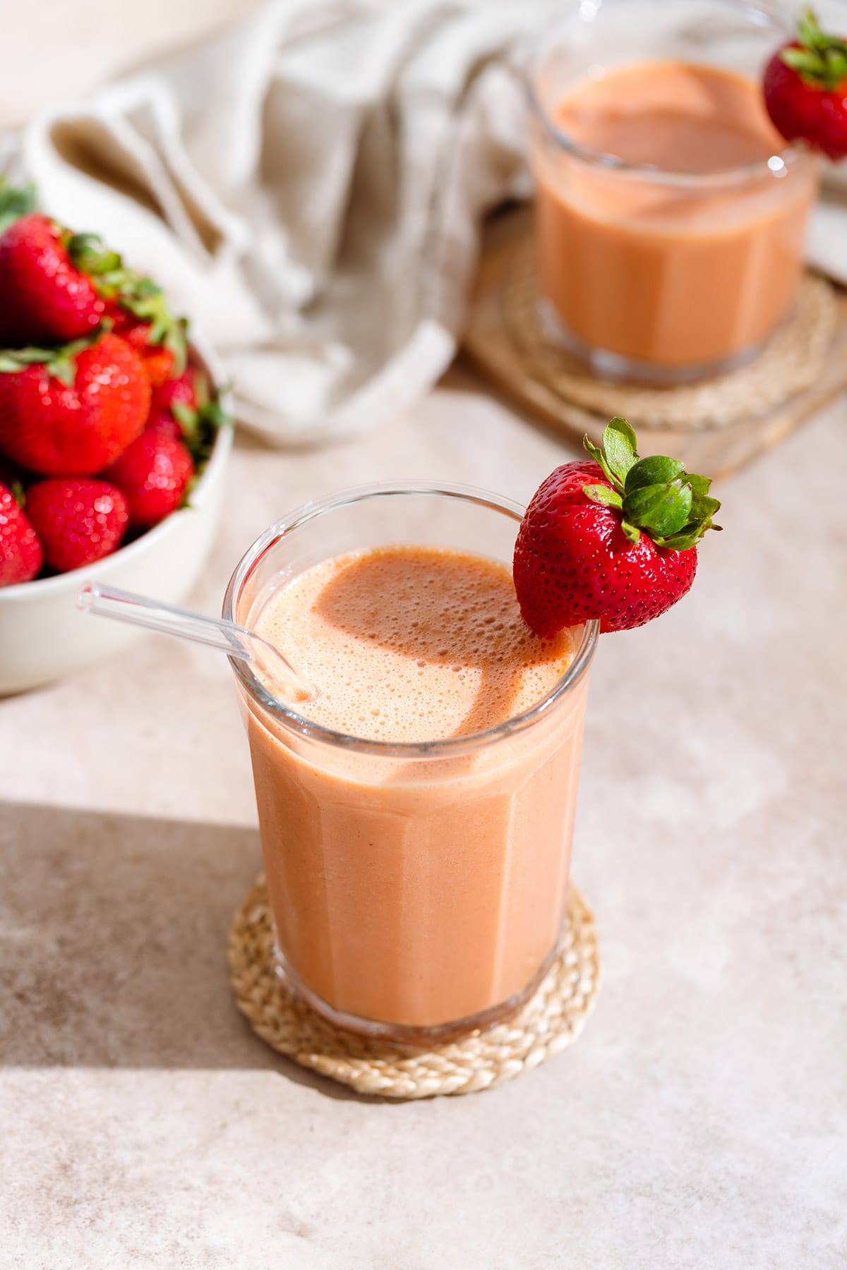 Peach strawberry smoothie in a tall glass with a glass straw and garnished with a fresh strawberry on the rim and more strawberries around it.