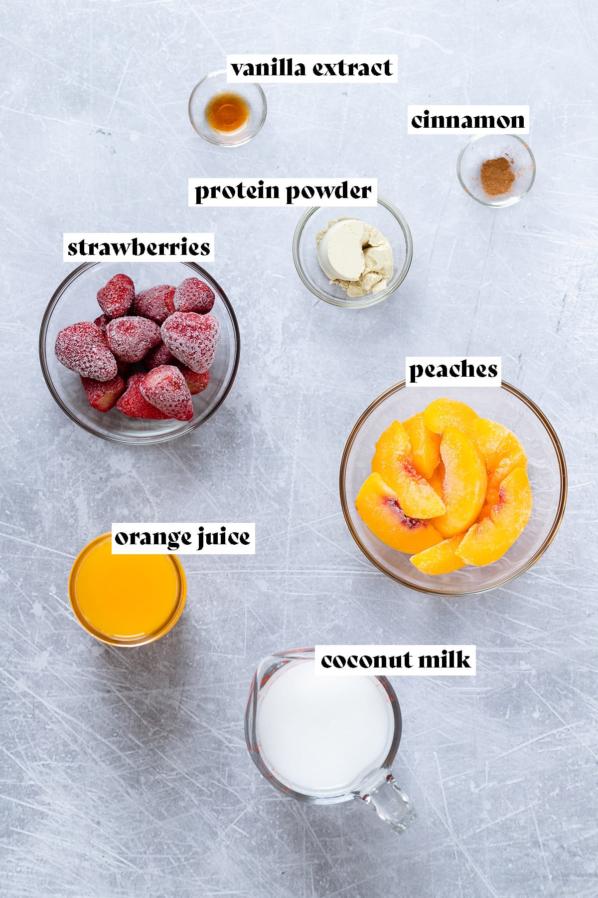 Ingredients for strawberry smoothie like frozen strawberries and peaches all laid out on a metal background.