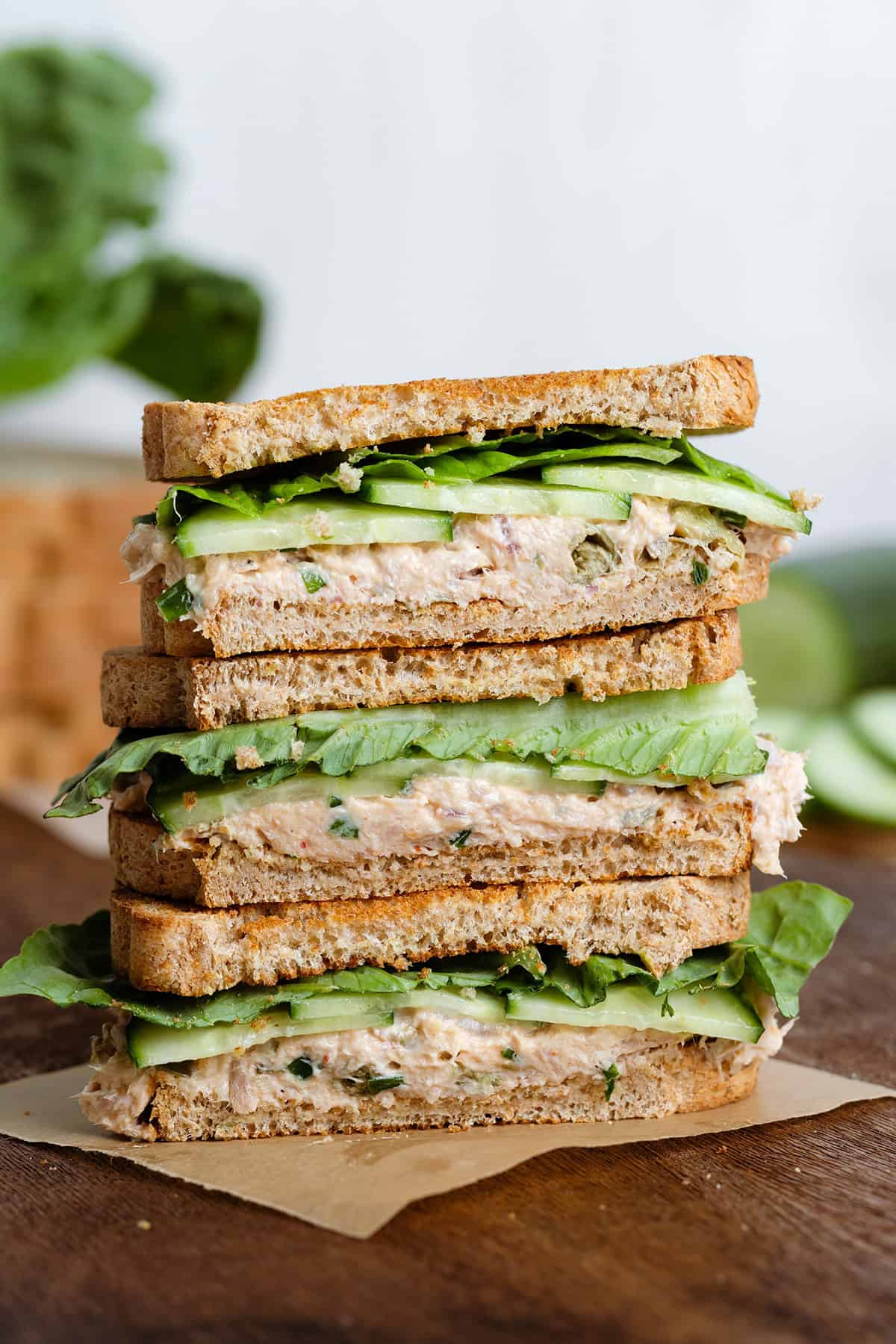 Tuna Cucumber Sandwiches stacked on a dark wooden cutting board.