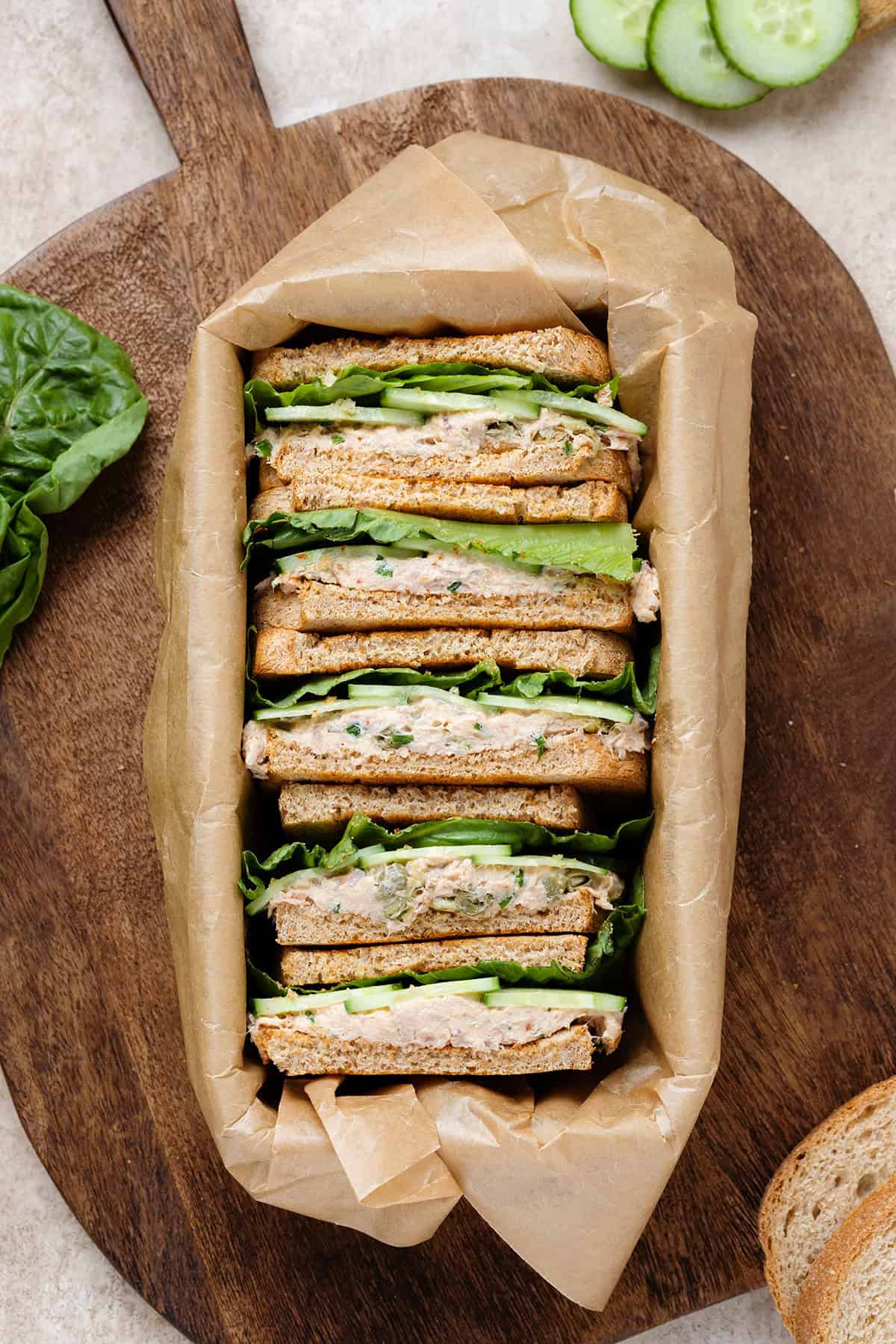 Tuna cucumber sandwiches packed in a box lined with parchment paper on a dark wooden cutting board.