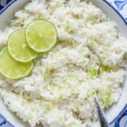Coconut lime rice garnished with lime slices in a white bowl with a blue edge on a blue tile background.