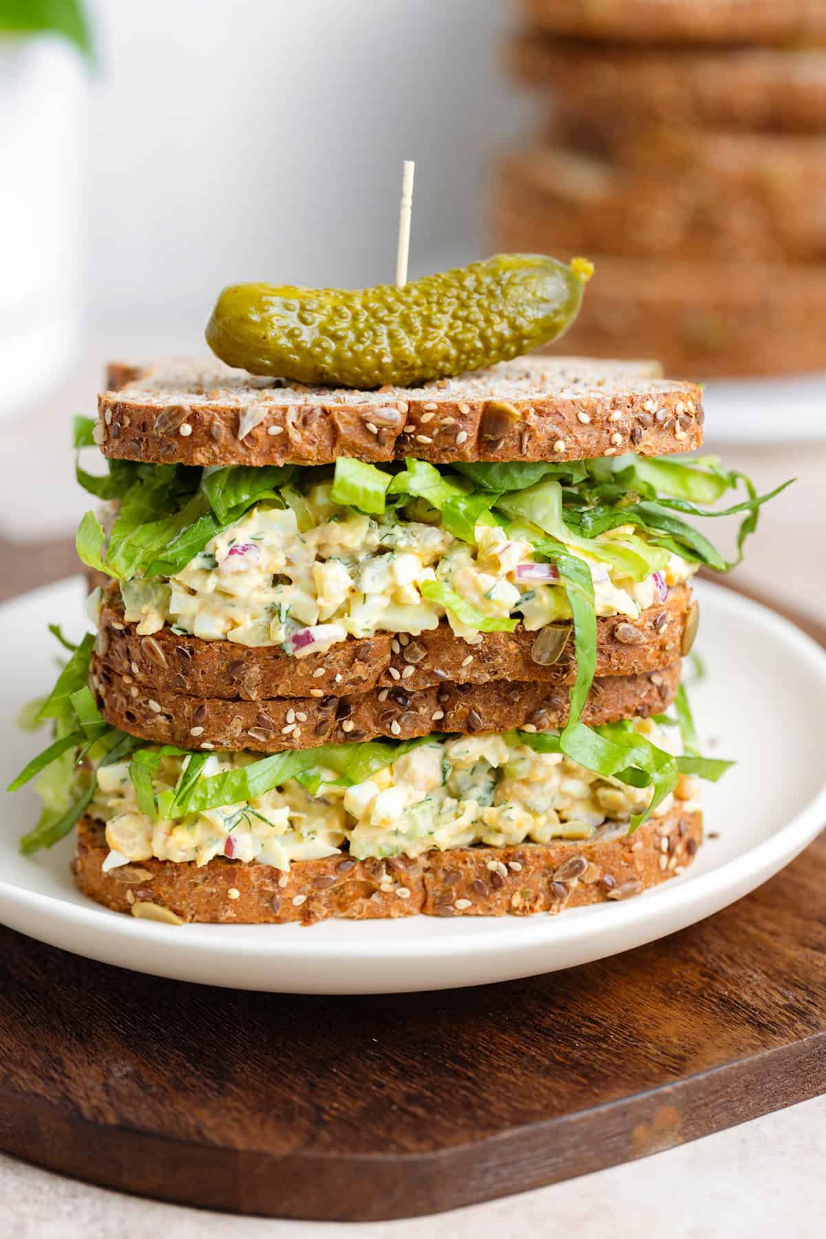 Two chickpea egg salad sandwiches on top of each other with a pickle on top.