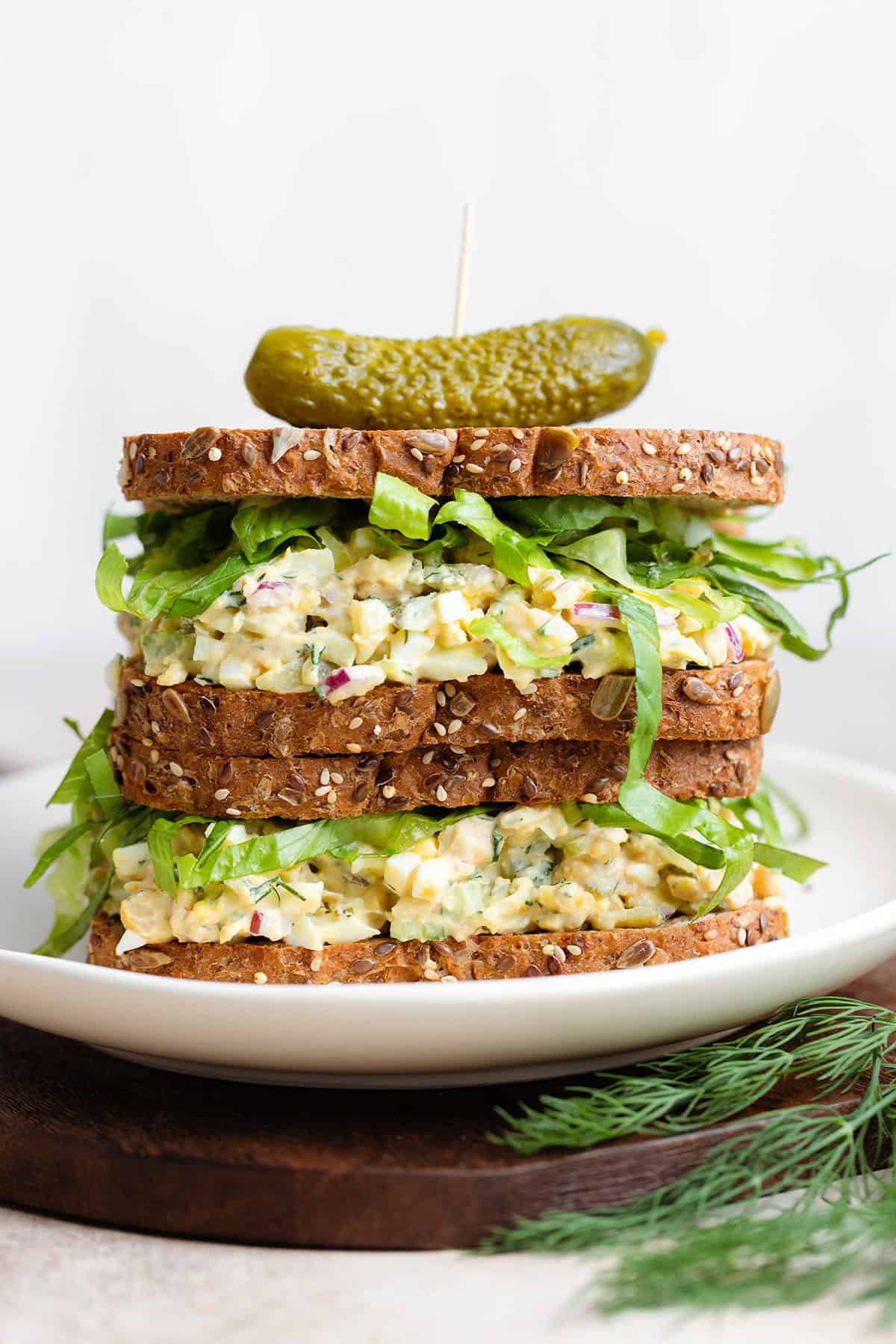 Two chickpea egg salad sandwiches on top of each other with a pickle on top.