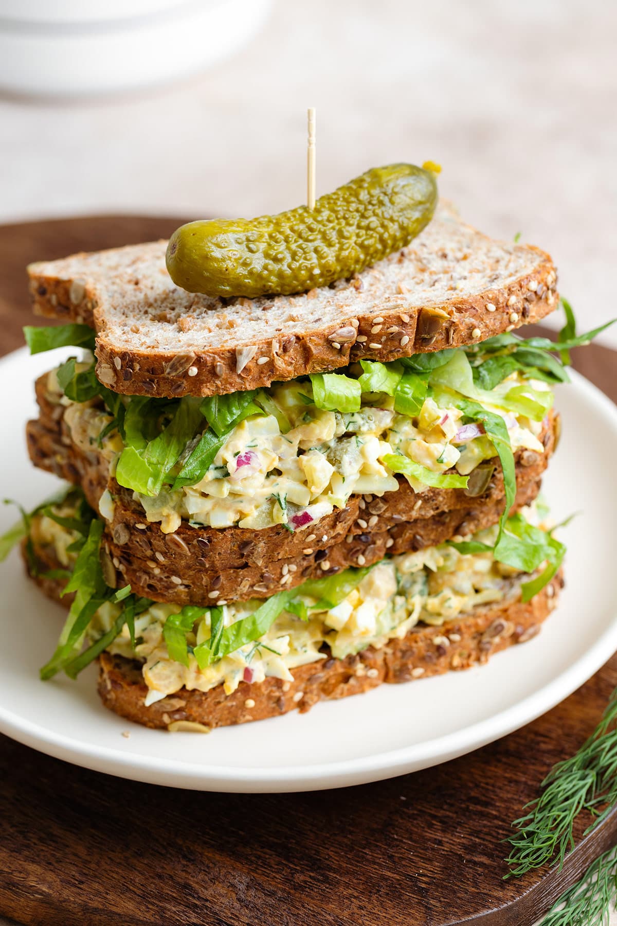 Two chickpea egg salad sandwiches on top of each other with a pickle on top.