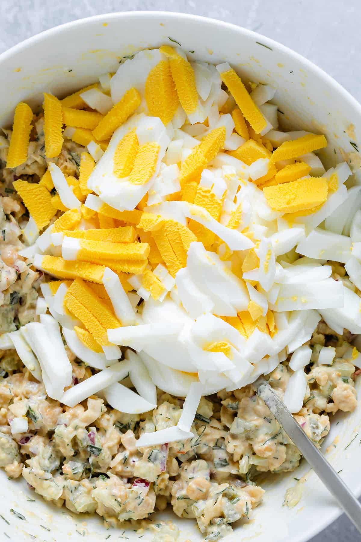 Chickpea egg salad with choped eggs on top in a large white bowl on a grey background.