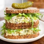 Two chickpea egg salad sandwiches on top of each other with a pickle on top.