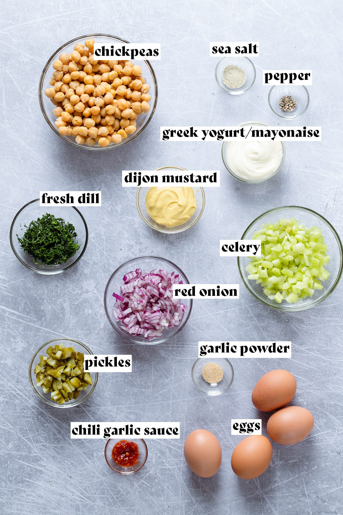 Chickpeas, eggs, celery and other ingredients for a chickpea egg salad sandwich ingredients laid out on a grey background.