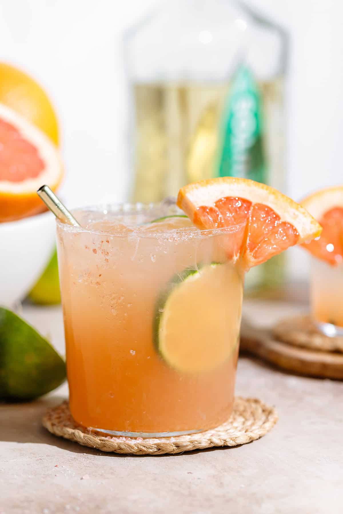 A paloma cocktail in a short glass garnished with salt, fresh lime, and grapefruit slices.