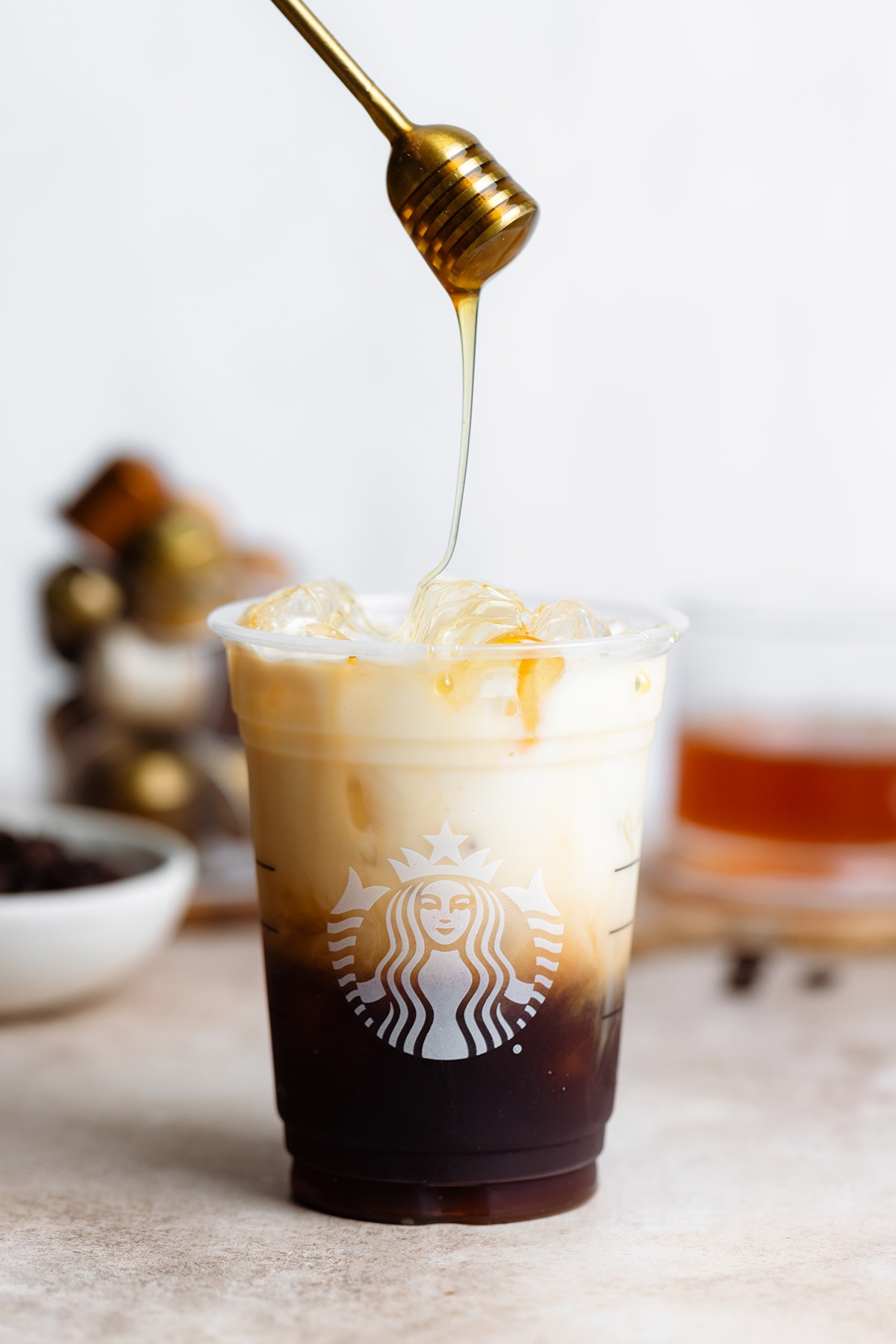 Honey being drizzled on iced coffee in a plastic cup.