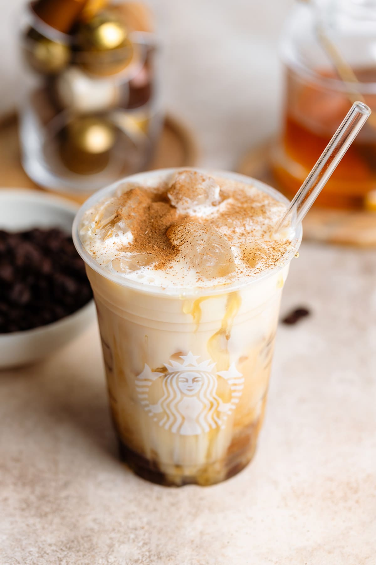 Almond milk slowly mixing into iced espresso in a plastic Starbucks cup with a glass straw and a cinnamon sprinkle on top.