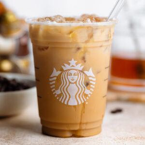 Iced coffee in a plastic Starbucks cup with a glass straw on a light orange background.