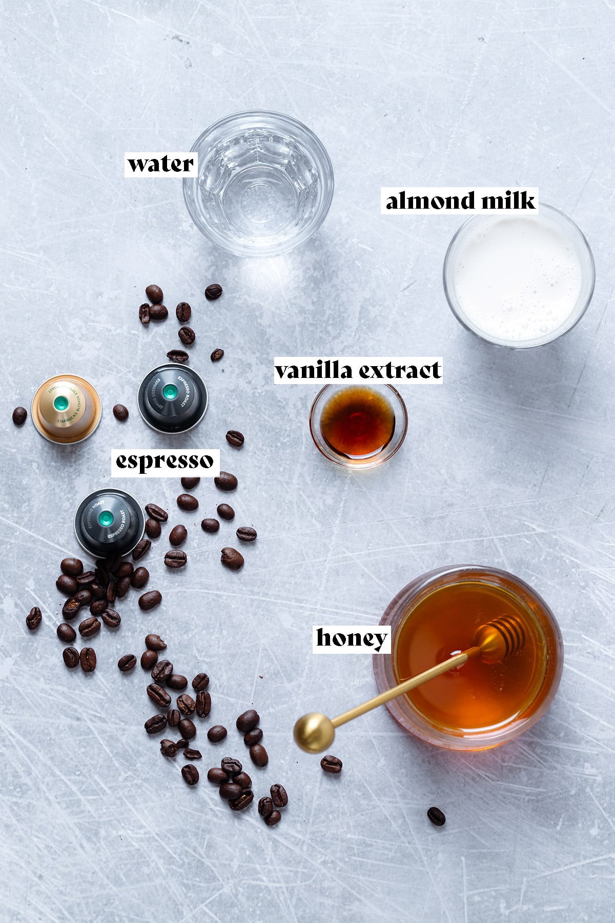 Ingredients for honey flat white like honey, espresso, and milk all laid out on a grey background.