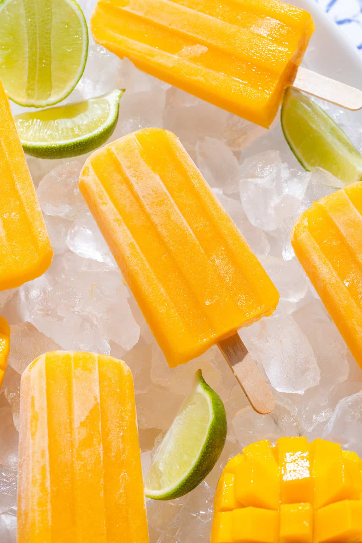 Bright orange mango popsicles on a white serving plate with ice and lime slices.