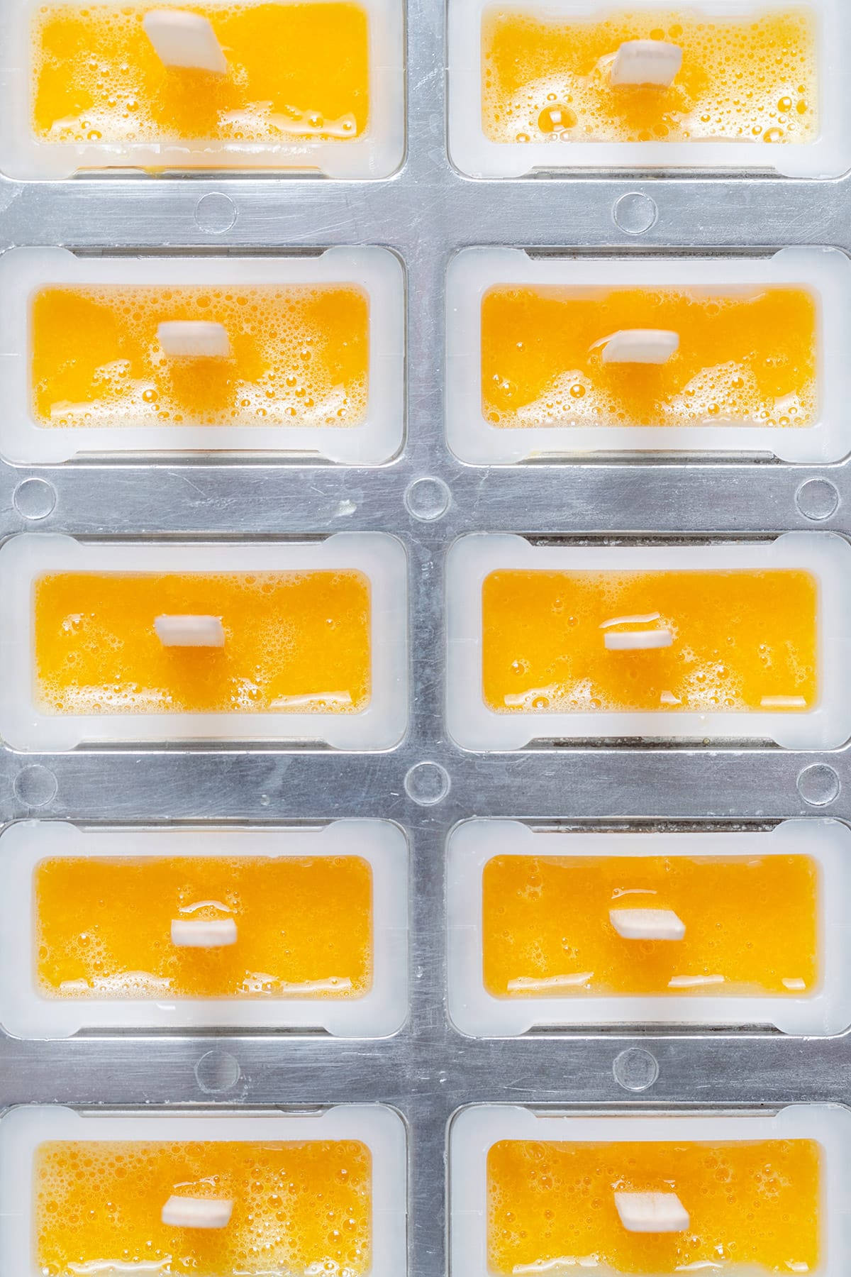 Ten mango popsicles in a popsicle moulds before freezing.