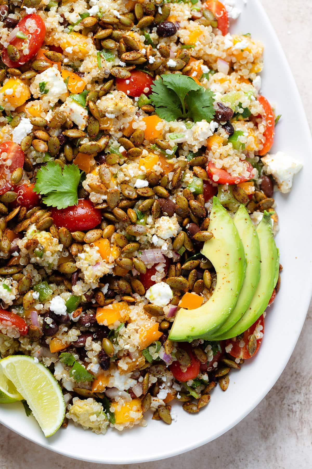 Mango quinoa salad topped with avocado slices on a large serving plate.