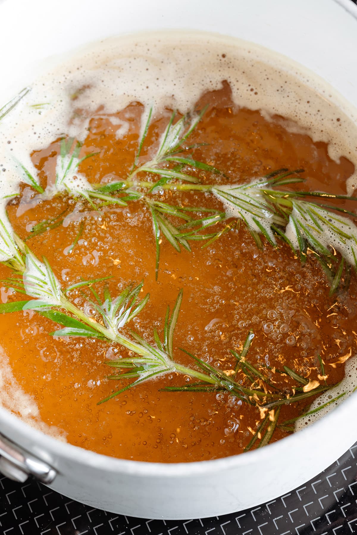 Rosemary syrup simmering in a white saucepan.