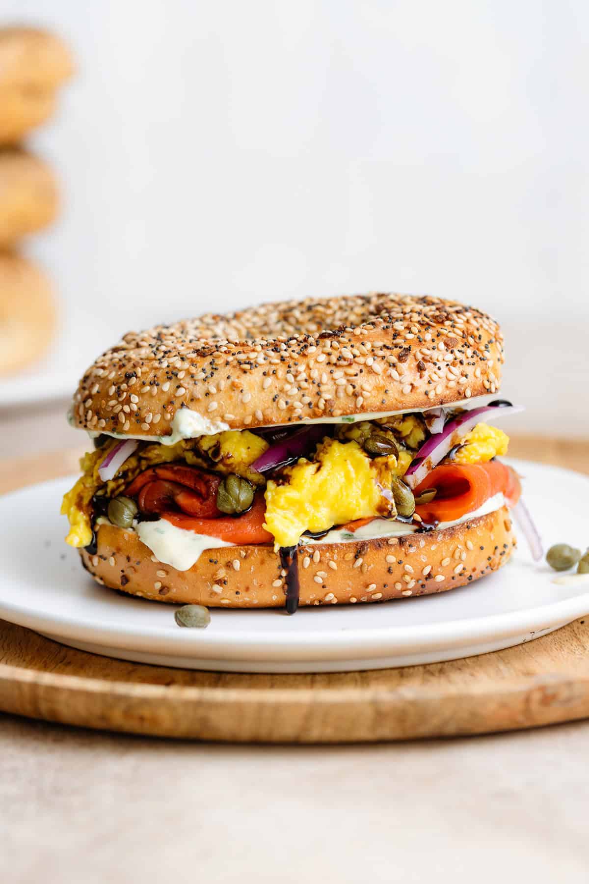 A toasted everything bagel with smoked salmon, scrambled eggs, cream cheese, capers, and red onion on a white plate.