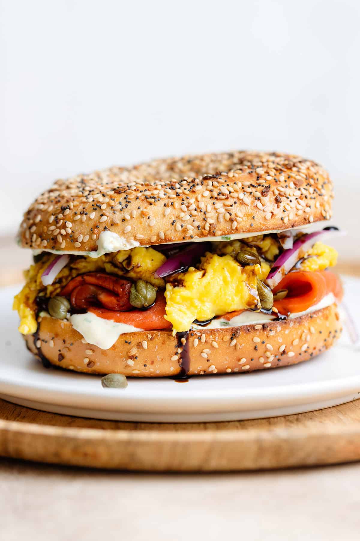 A toasted everything bagel with smoked salmon, scrambled eggs, cream cheese, capers, and red onion on a white plate.