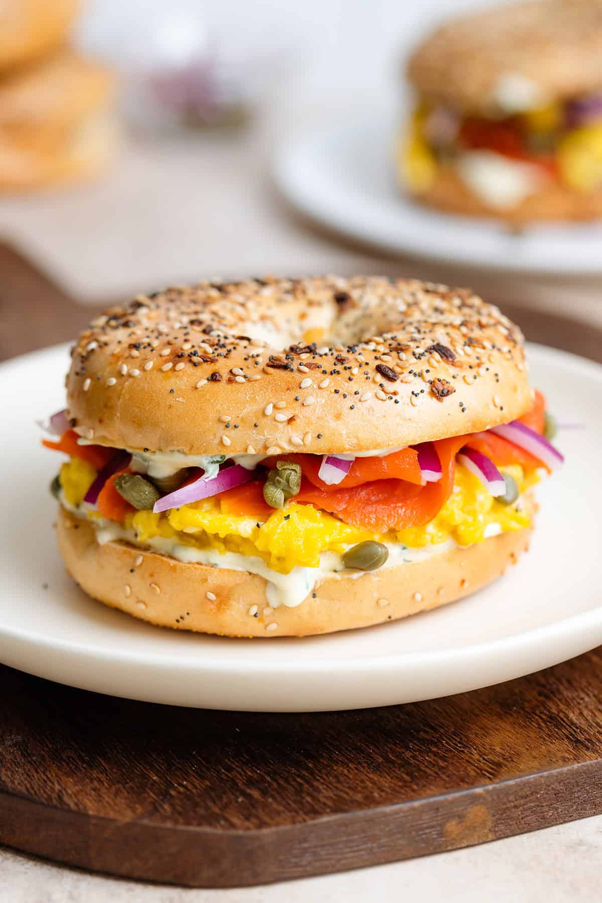 A toasted everything bagel with smoked salmon, scrambled eggs, cream cheese, capers, and red onion on a white plate.