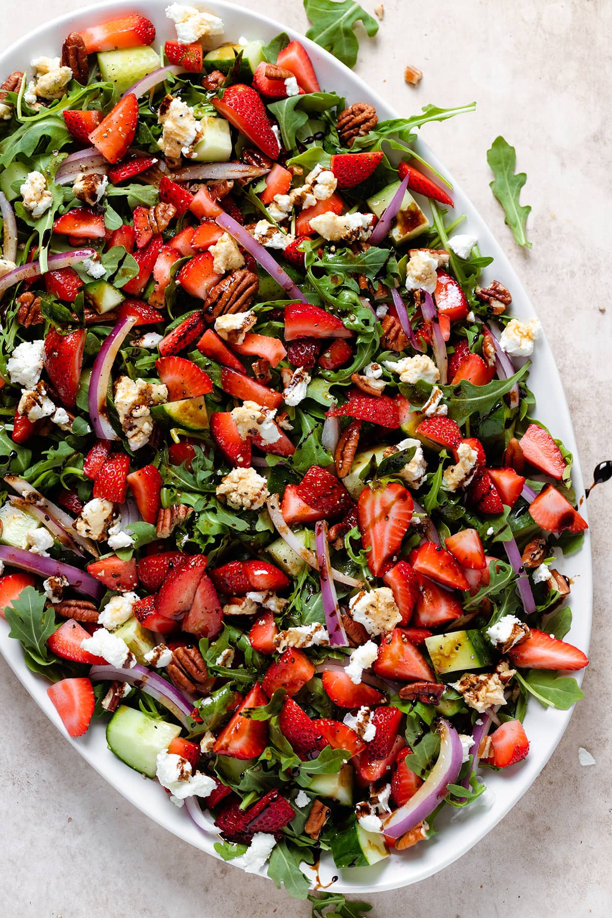 Strawberry goat cheese salad drizzled with balsamic glaze on a large white plate.