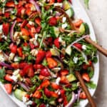 Strawberry goat cheese salad drizzled with balsamic glaze on a large white plate with wooden serving spoons.