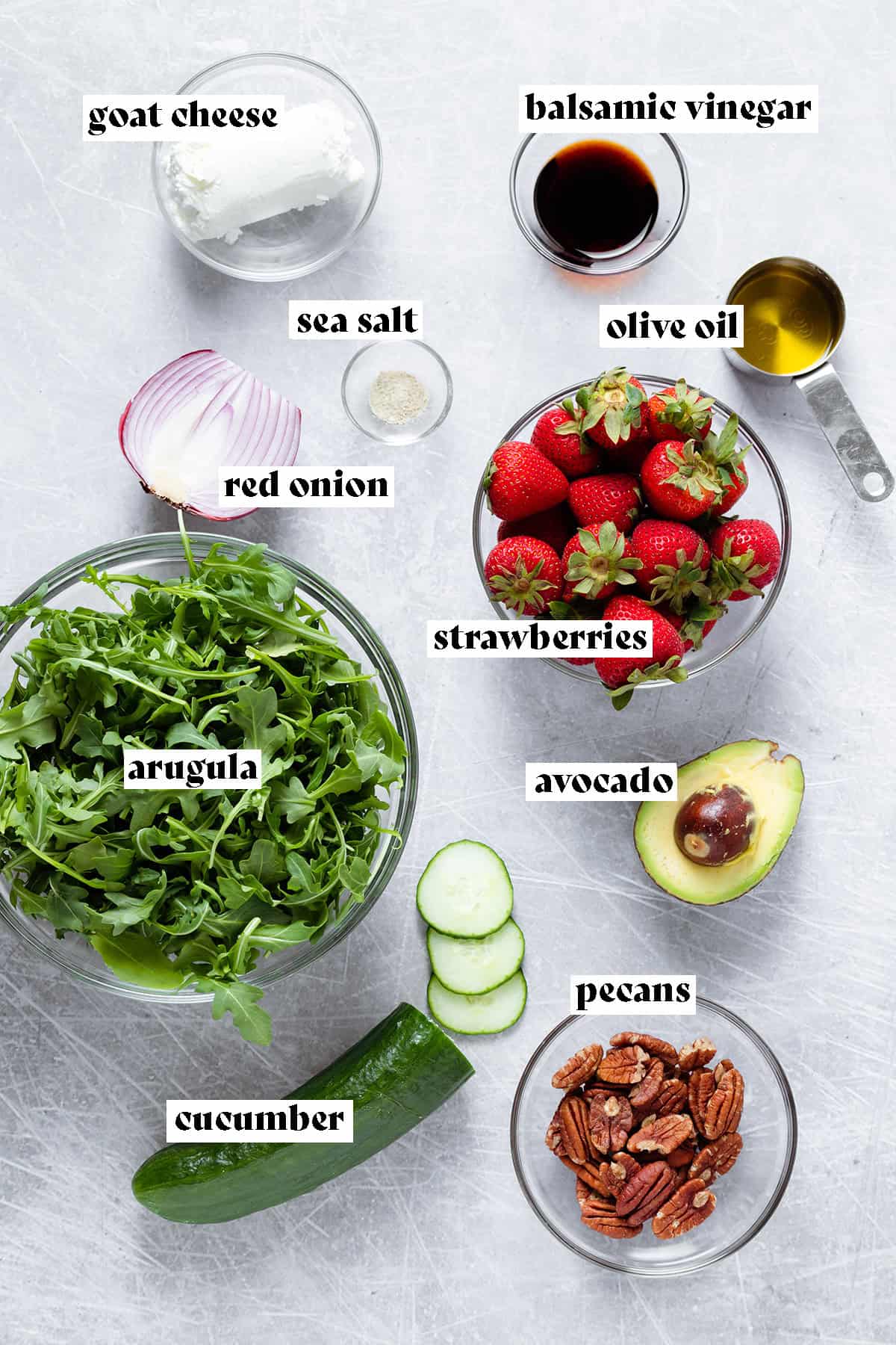 Ingredients for strawberry salad like strawberries, arugula, goat cheese, and cucumber, all laid out.