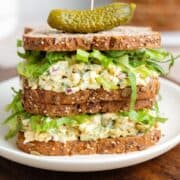 Two chickpea egg salad sandwiches on top of each other with a pickle on top.