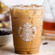 Iced coffee in a plastic Starbucks cup with a honey drizzle and a glass straw.