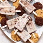 Cookie-dough popsicles arranged on a white serving platter filled with ice and chocolate cookies.