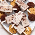 Cookie-dough popsicles arranged on a white serving platter filled with ice and chocolate cookies.