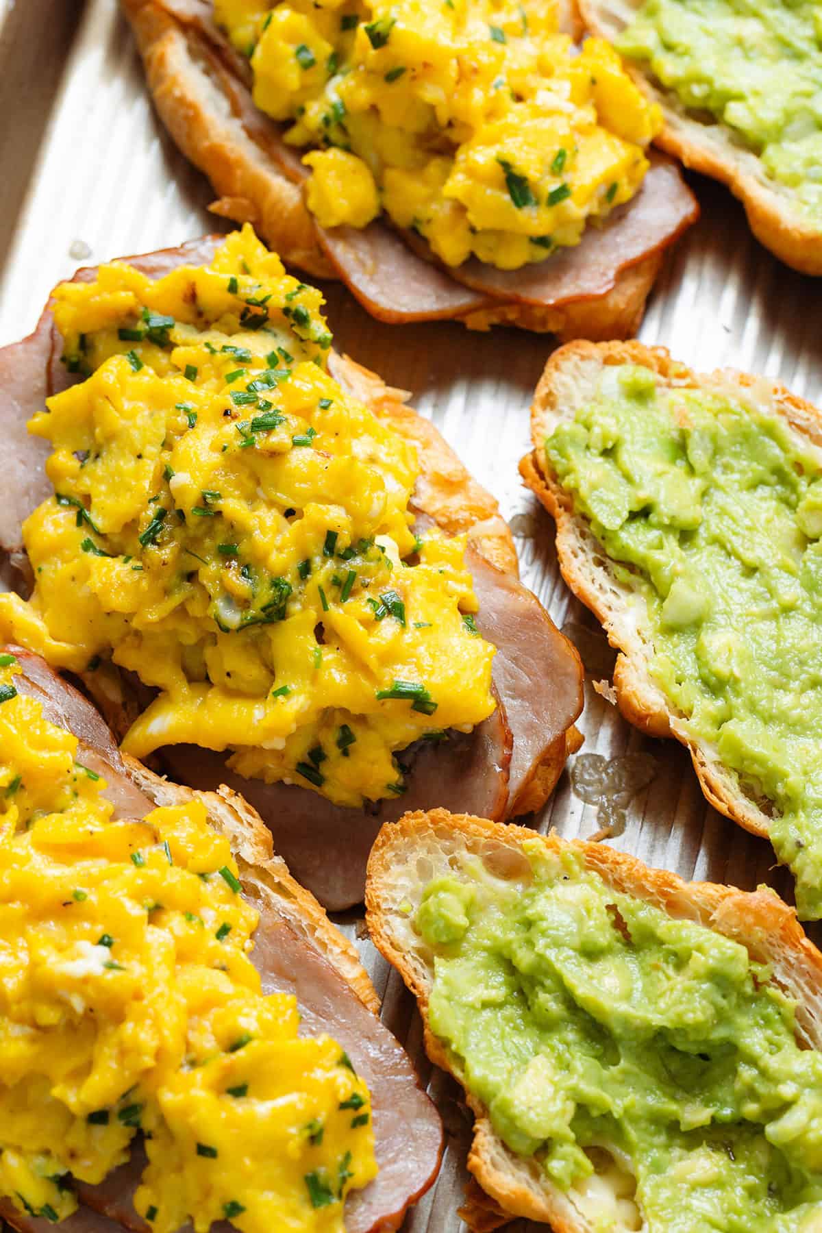 Three toasted croissants on a baking sheet filled with turkey bacon, scrambled eggs, and guacamole.