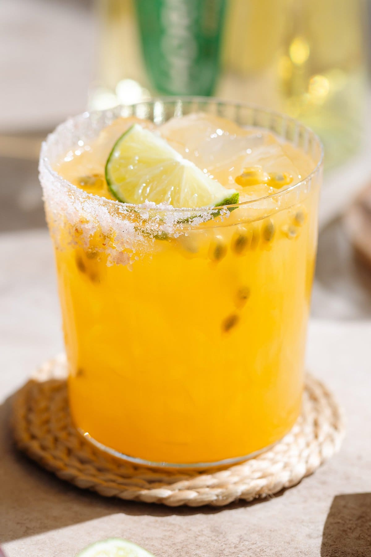 Bright yellow passion fruit margarita in a short salt-rimmed glass with ice and garnished with a slice of lime.