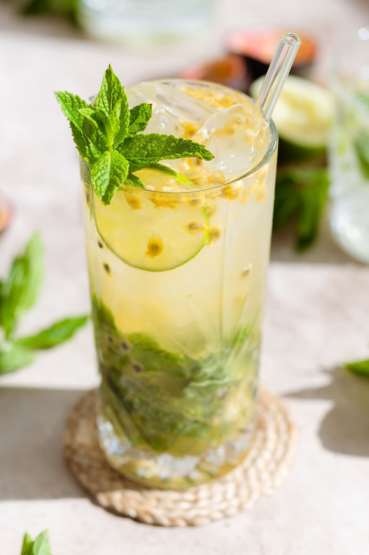 Passion fruit mojito in a tall glass with a glass straw garnished with fresh mint, lime, and passion fruit.