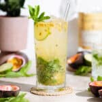 Passion fruit mojito in a tall glass with a glass straw garnished with fresh mint, lime, and passion fruit.