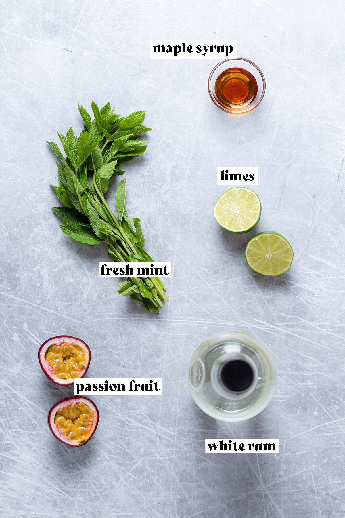 Ingredients for a passion fruit mojito like fresh mint and lime all laid out on a metal background.