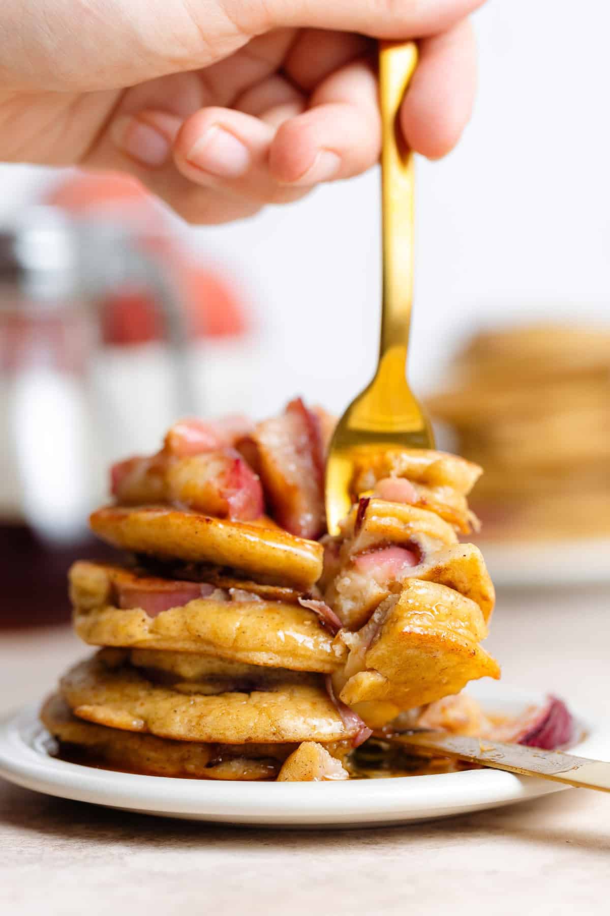 Pancakes stuffed with peaches stacked on a white plate being cut into with gold cutlery.