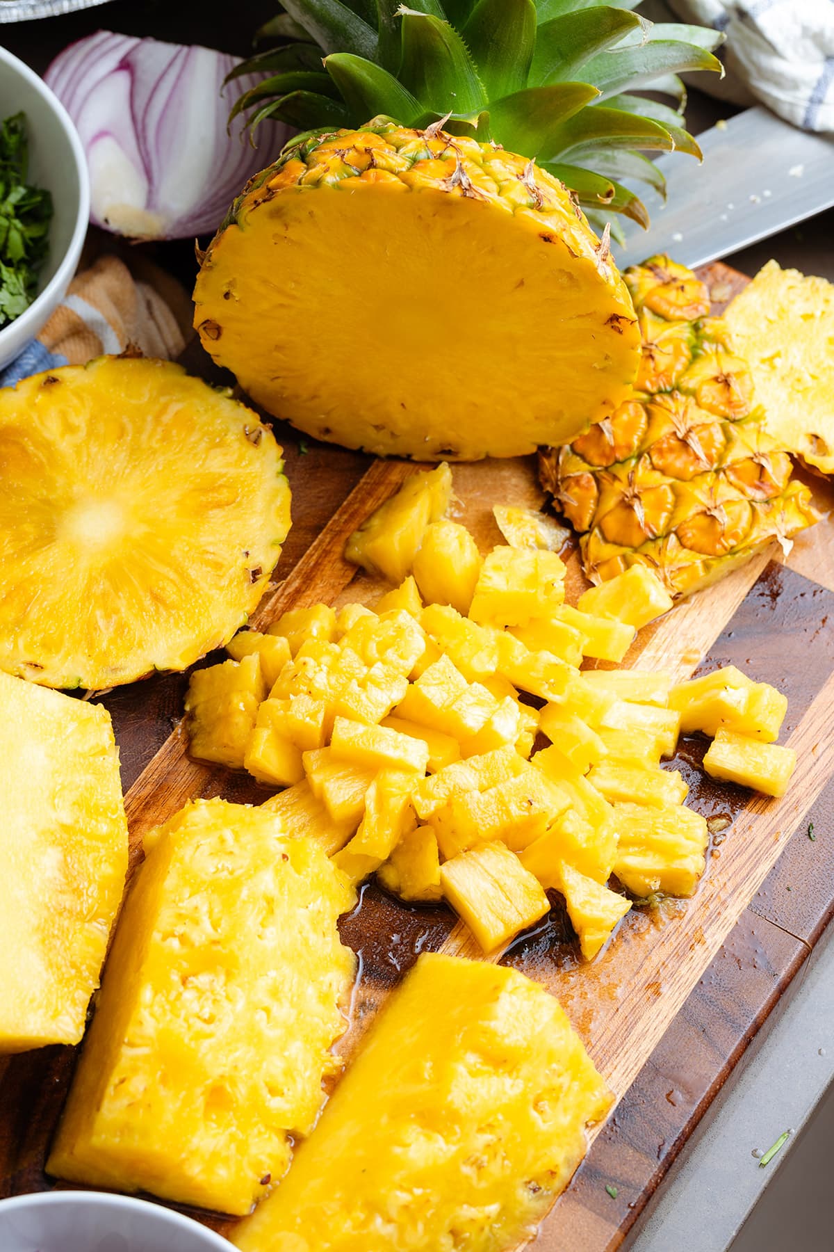 Sliced and diced pineapple on a wooden cutting board in the process of being diced.