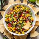 Colorful pineapple pico de gallo in a white bowl on a black plate with tortilla chips.