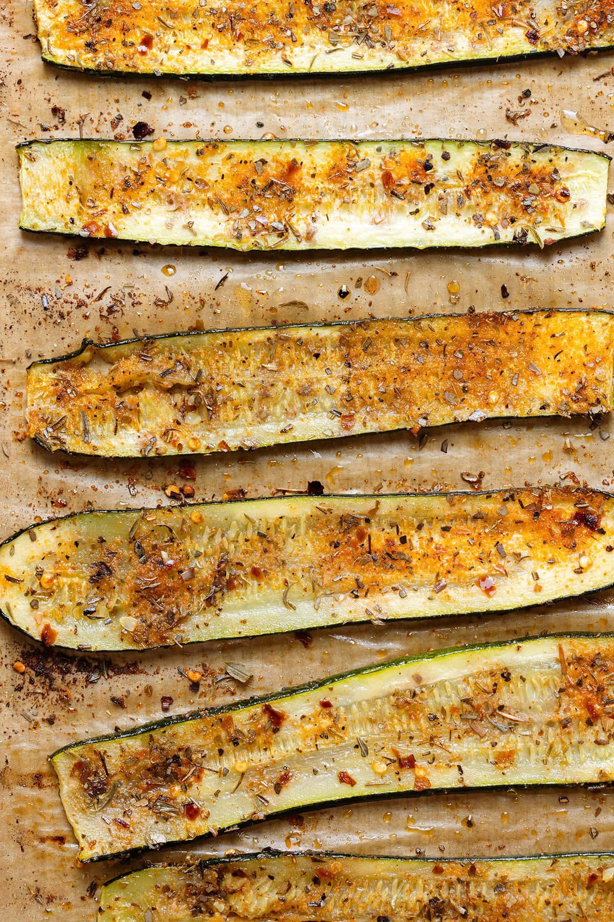 Roasted zucchini slices with lots of spices in a single layer on parchment paper.