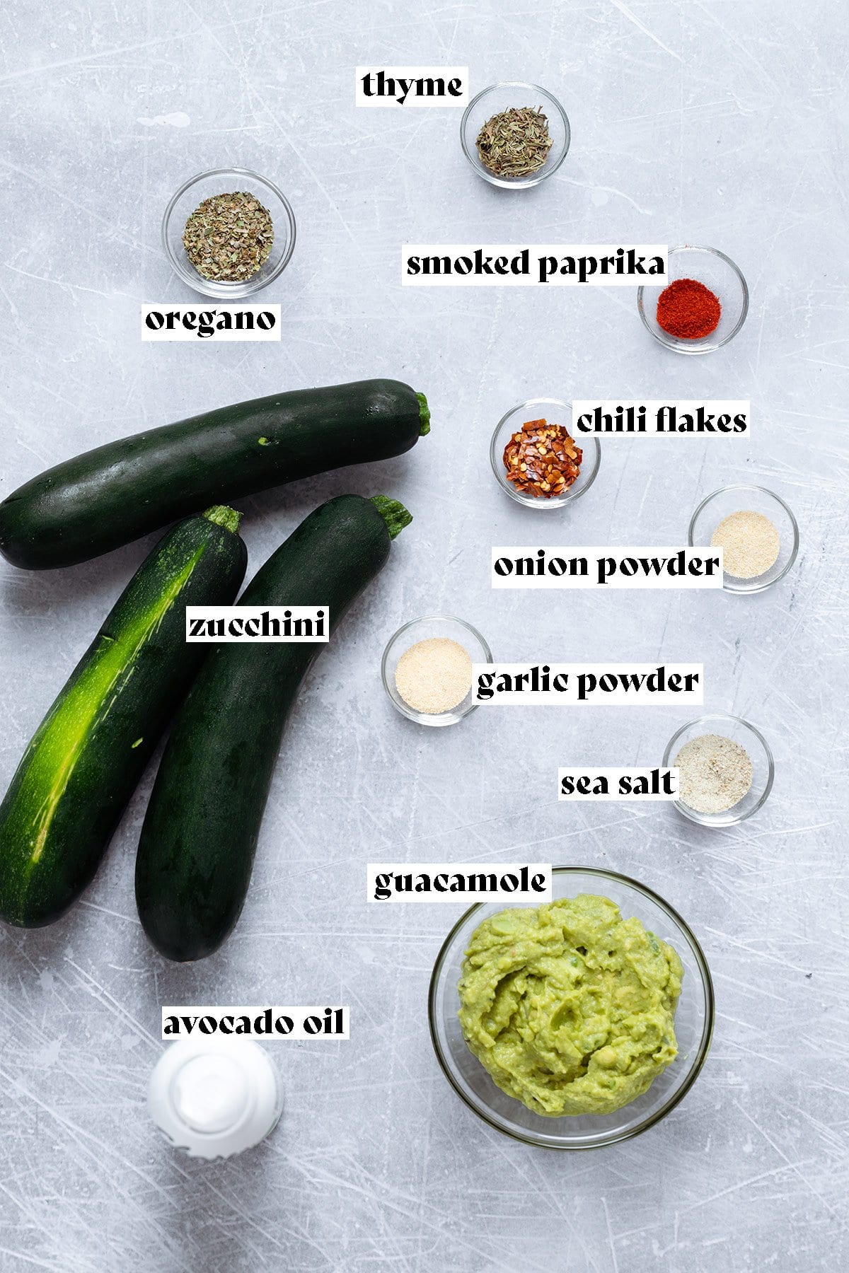 Ingredients for zucchini rolls like zucchini and guacamole laid out on a metal background.