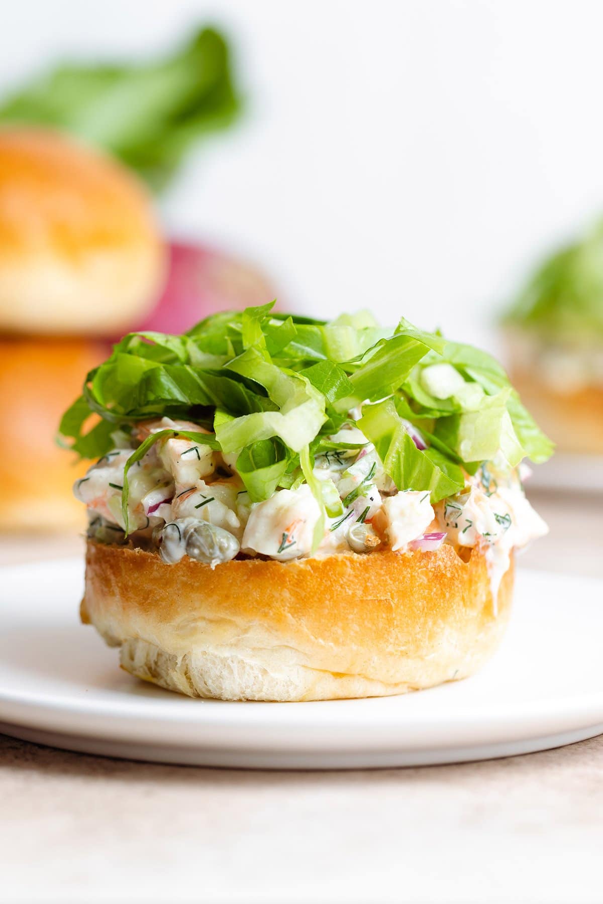 A bottom of a toasted brioche bun with creamy shrimp salad and shredded romaine lettuce on top.