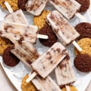 Cookie-dough popsicles arranged on a white serving platter filled with ice and chocolate cookies.