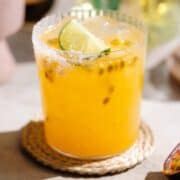 Bright yellow passion fruit margarita in a short salt-rimmed glass with ice and garnished with a slice of lime.