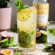 Passion fruit mojito in a tall glass with a glass straw garnished with fresh mint, lime, and passion fruit.