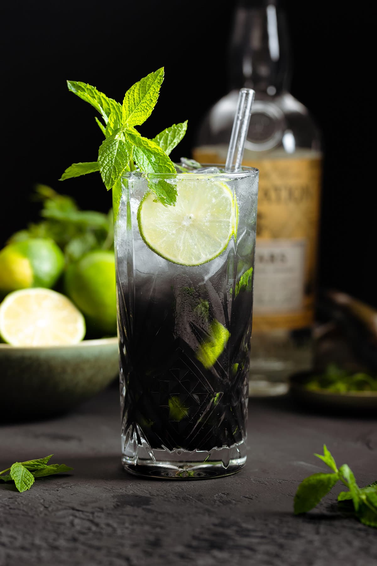 Black mojito with sparkling water on top creating an ombre effect in a tall glass garnished with a slice of lime and fresh mint.